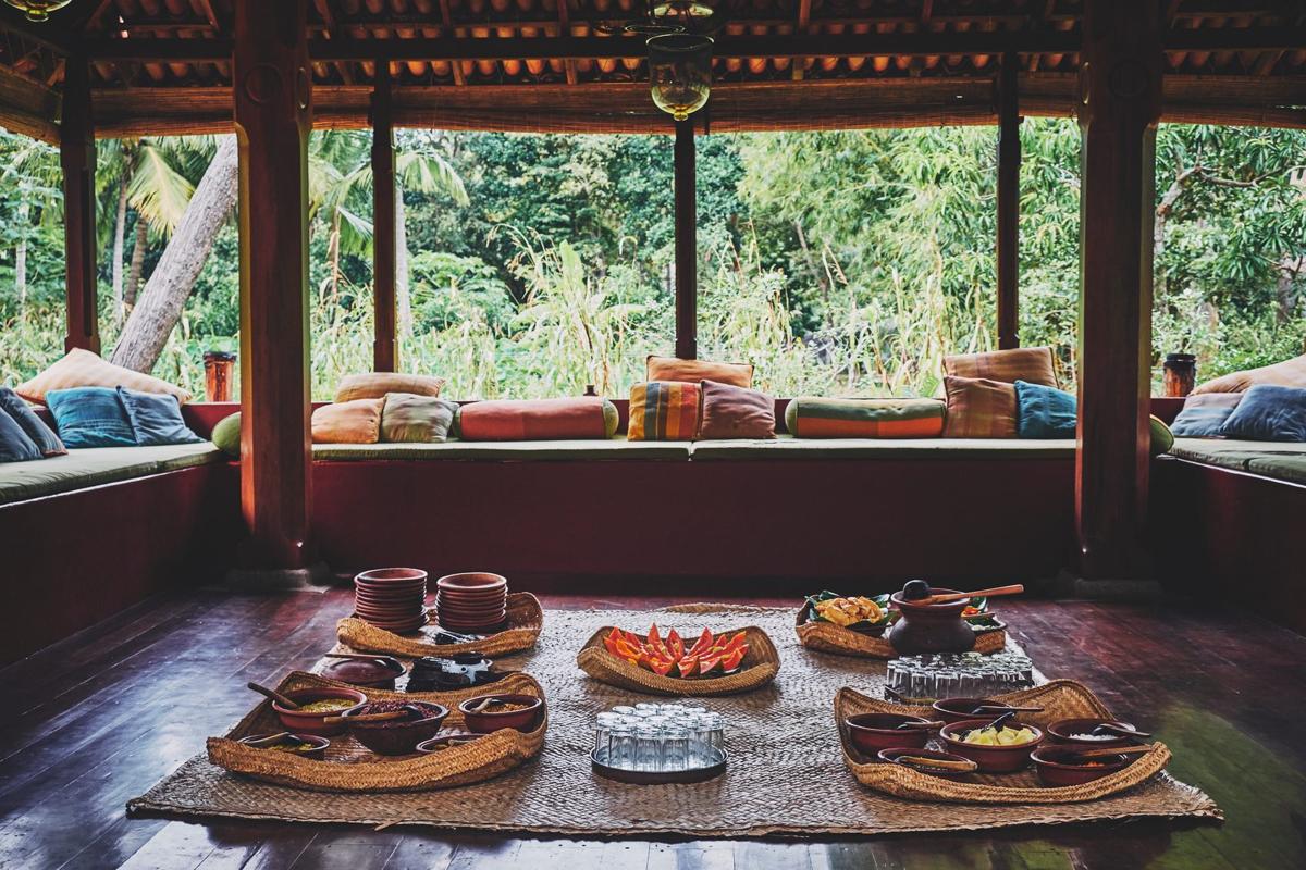 Lunch laid out in the open Ambalama pavilion: clay pots and woven trays on low tables, paddy fields and jungle beyond the pillars