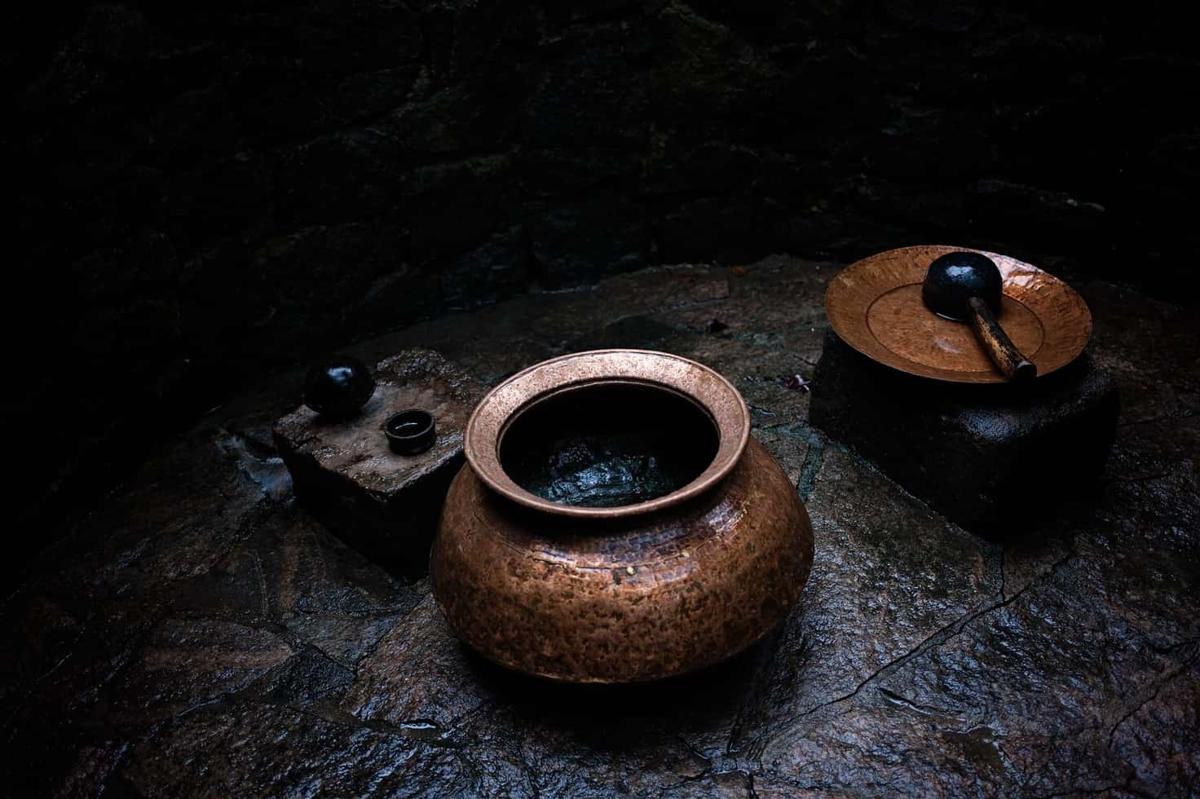 A hammered copper pot and bowl with a wooden ladle on the wet stone floor of the open-air bathing enclosure