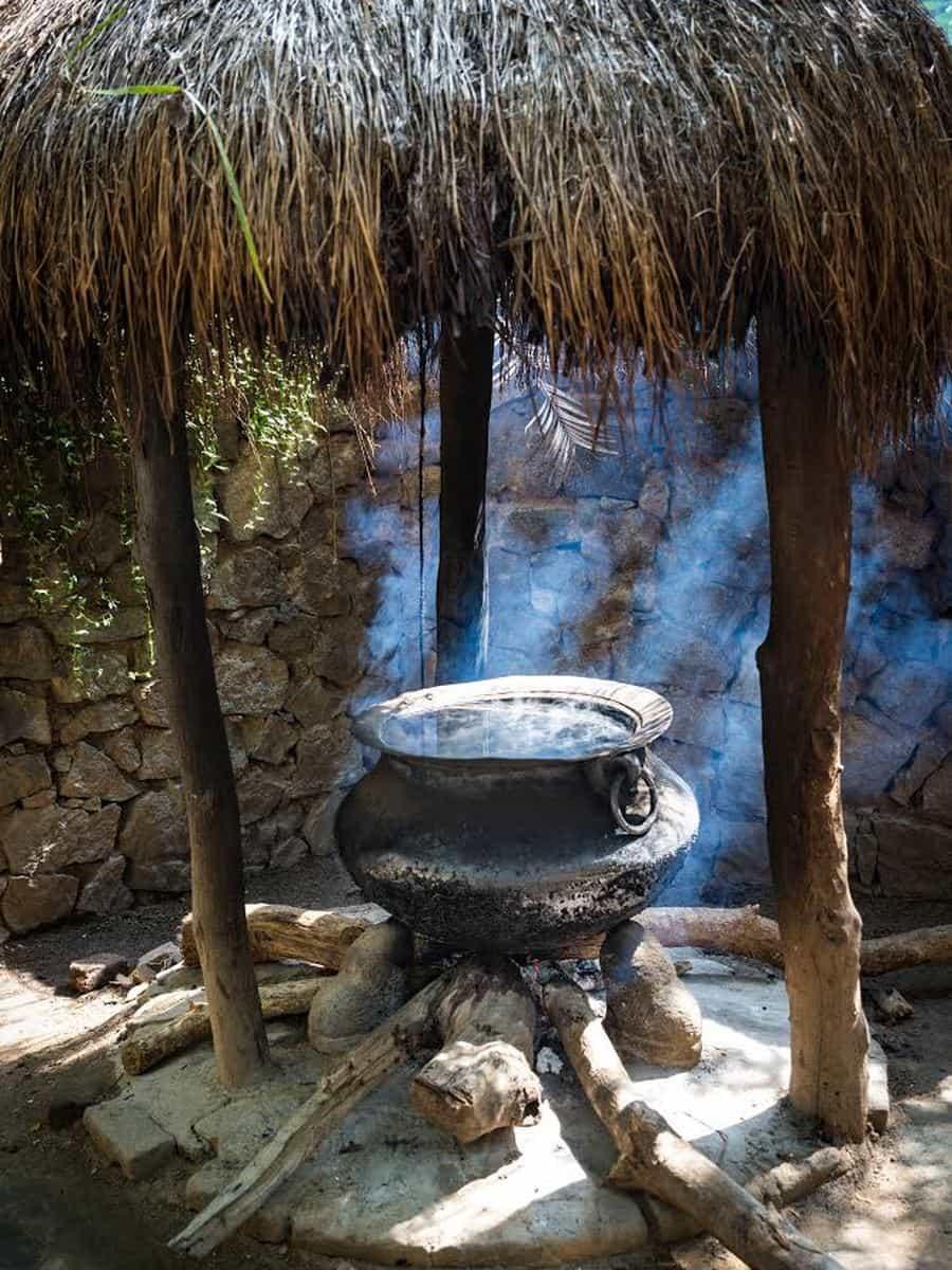 The clay pot over the wood fire under its thatched roof, steam rising from the water