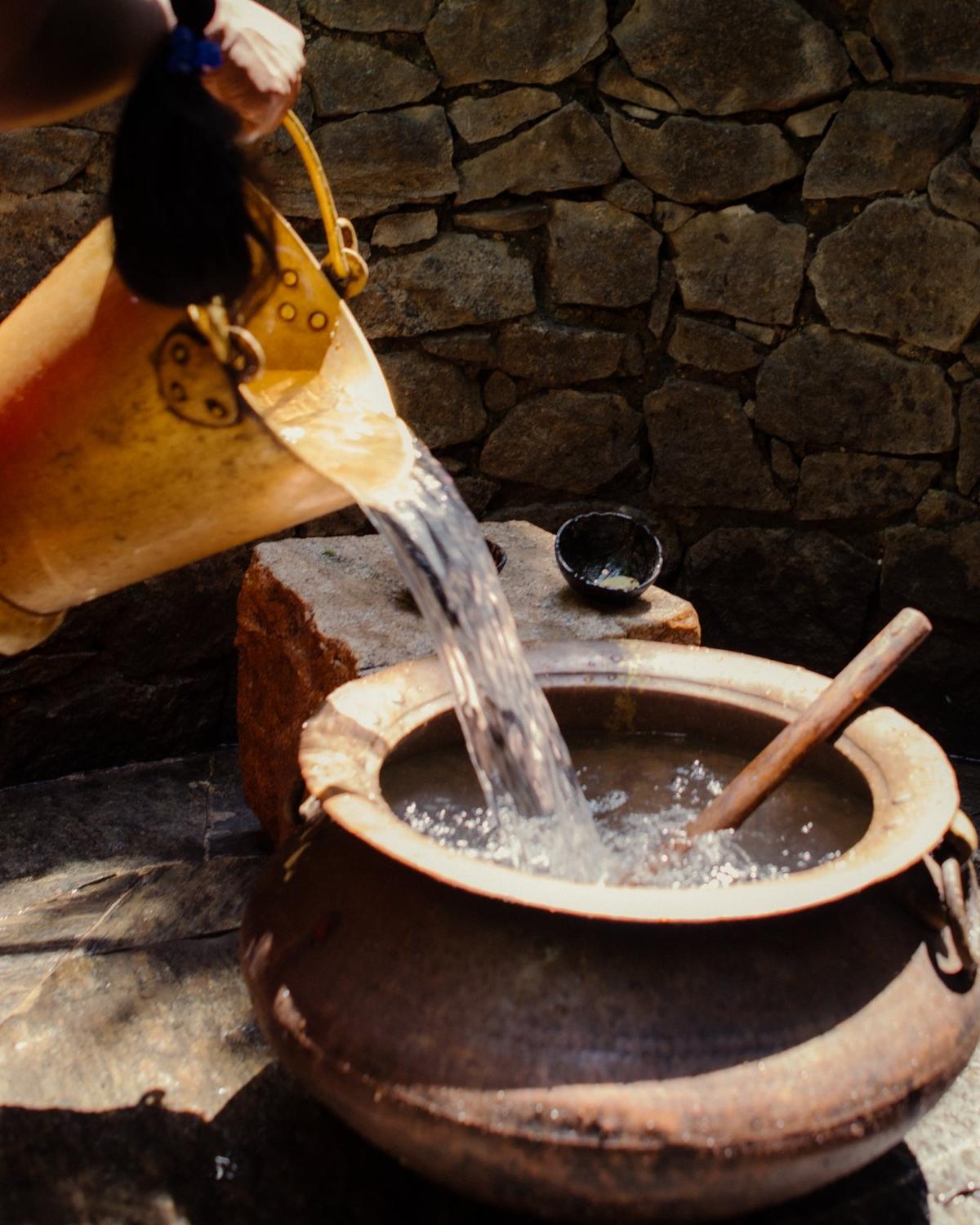 A therapist in white strikes a bronze singing bowl resting on a guest's chest in an open Ayurveda pavilion at Ulpotha, Sri Lanka.