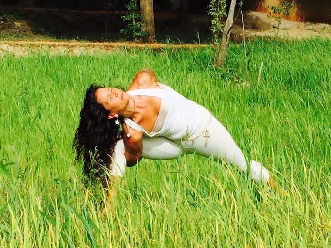 A woman stretching over a cork block on an orange mat in the open-sided shala, polished wood floor and jungle all around