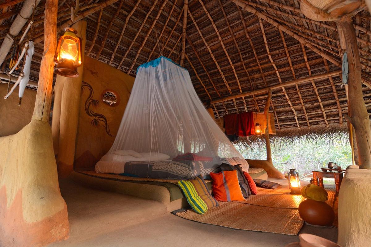 A wattle-and-daub hut at nightfall: the bed under its white mosquito net, a lantern glowing by the earthen wall, the jungle dark outside