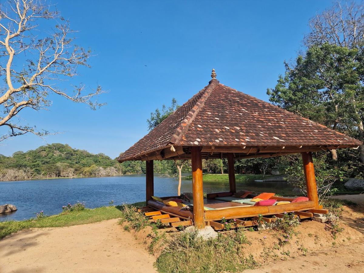 A tiled-roof pavilion with cushioned daybeds on the shore of the lake, under a clear blue sky