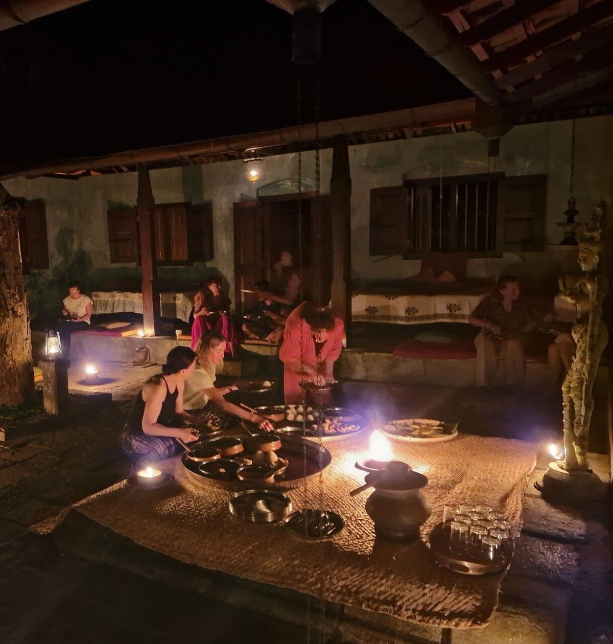 Dinner by lamplight: guests seated on the floor of the pavilion around dishes and oil lamps