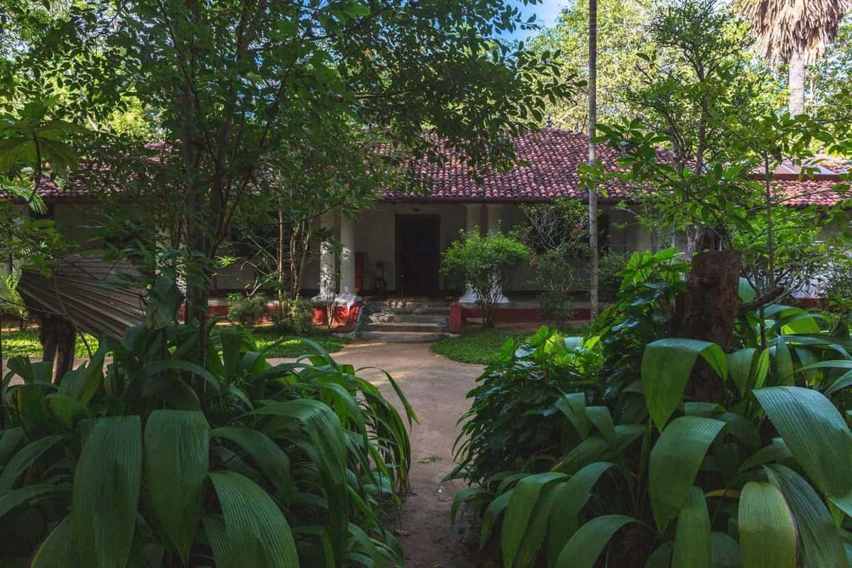 The white walawwa with its red clay-tile roof, glimpsed down a sand path through deep-green tropical foliage