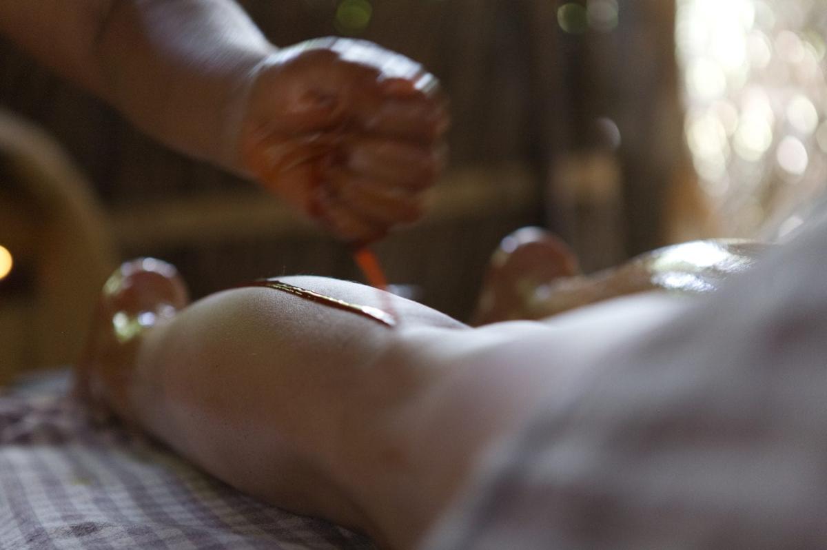A therapist pours warm herbal oil in a thin stream onto a guest's back at Ulpotha, Sri Lanka.