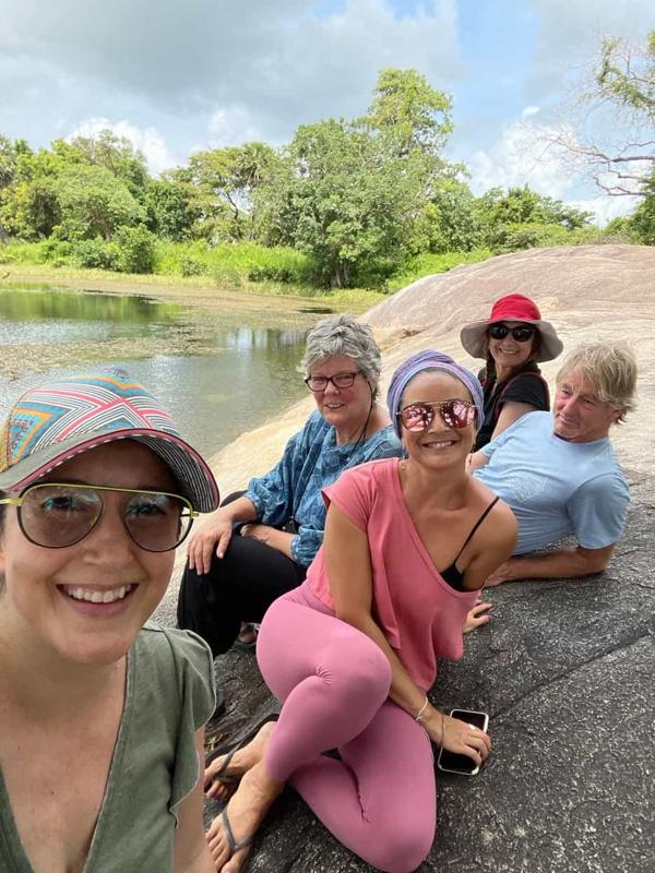 Smiling guests in sun hats on a rock by the lake