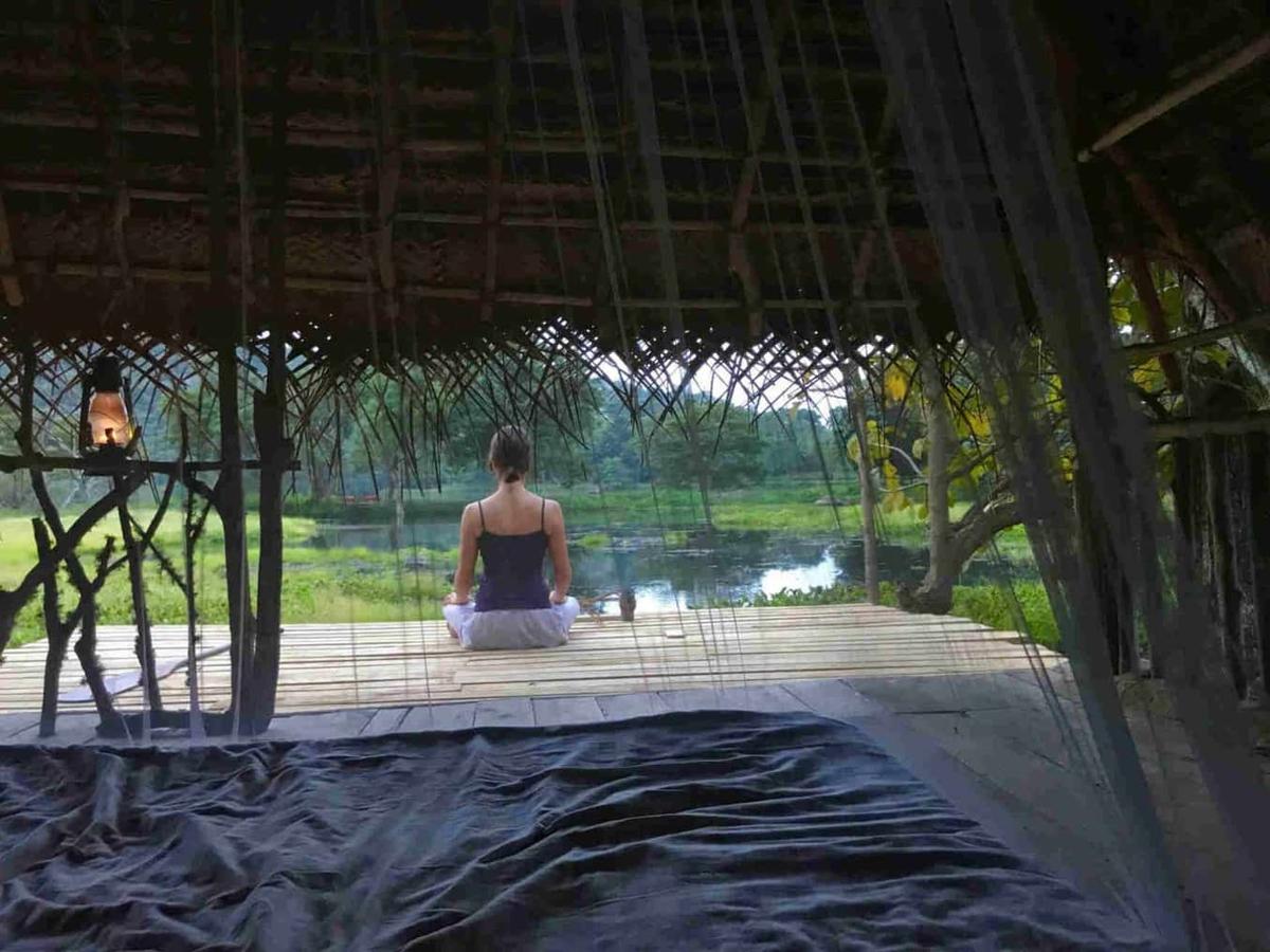 A woman meditating on a bamboo deck over the lake at first light, a lantern beside her.
