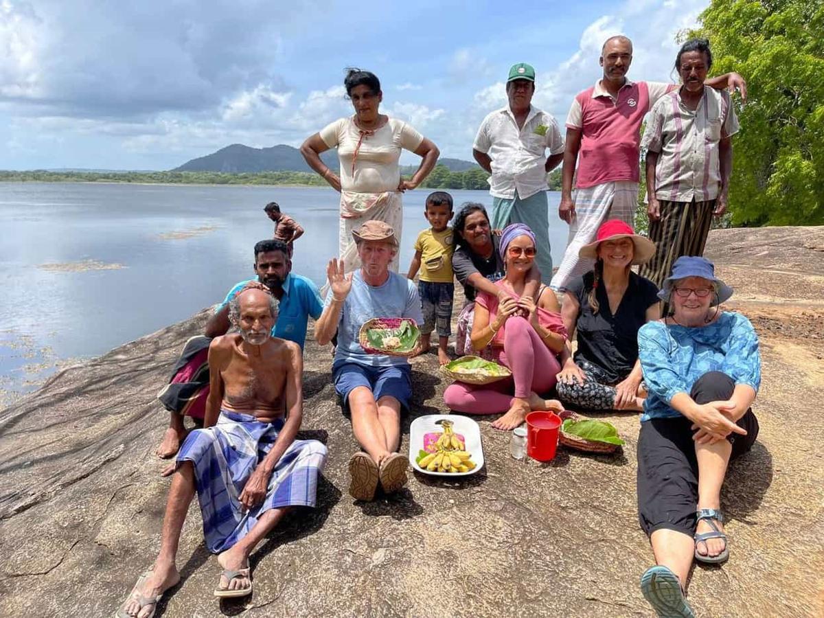Villagers and guests sharing food on a rock by the lake at Ulpotha.